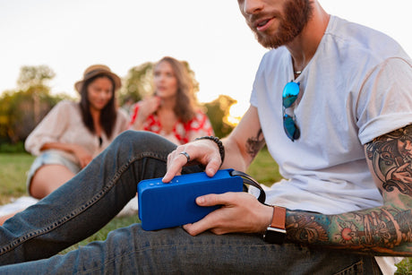 Junger Mann mit blauem Bluetooth-Lautsprecher beim Picknick mit Freunden im Park